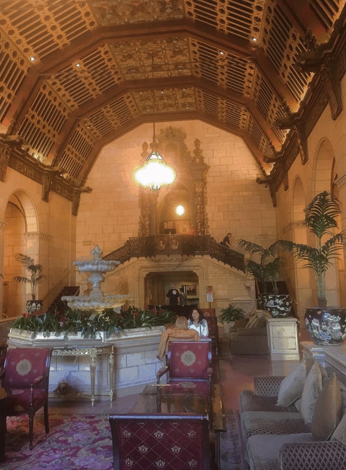 An ornate hotel lobby with a painted beamed ceiling, a fountain and a chandelier