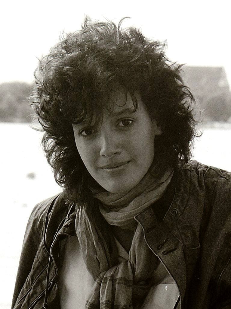 Jennifer Beals, nineteen, with a mass of dark curls, a check scarf and a dark jacket, by the water