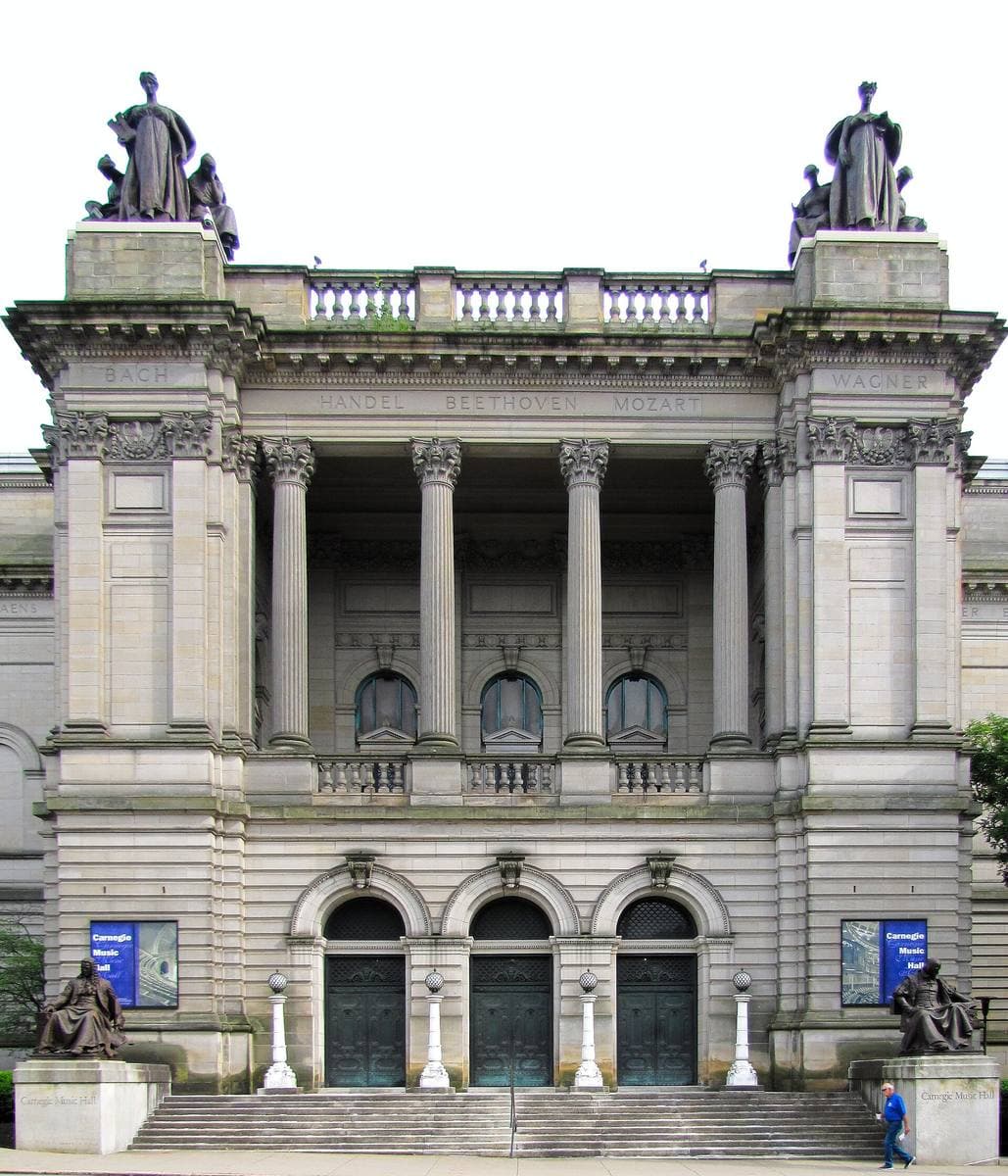 A grey stone classical front with paired columns and statues on the roofline