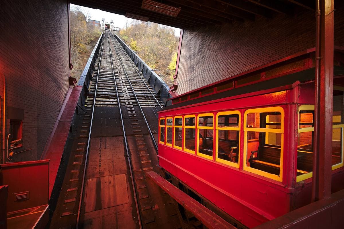 A red wooden incline car with lit windows beside the steep track up Mount Washington