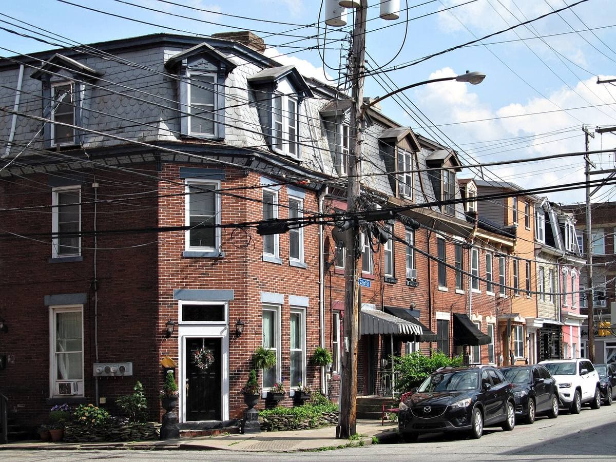 A row of brick houses with slate mansard roofs, cars parked along the kerb