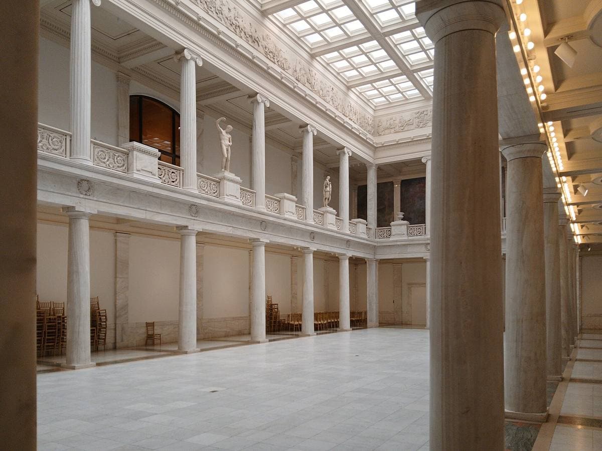 A white marble hall with a gallery of columns round a bright, empty floor
