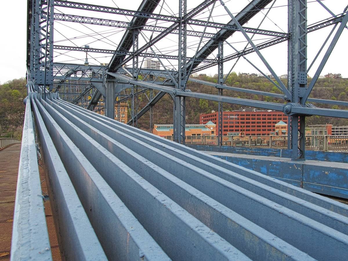 Ribbed steel and blue trusses of the Smithfield Street Bridge, the river bank beyond