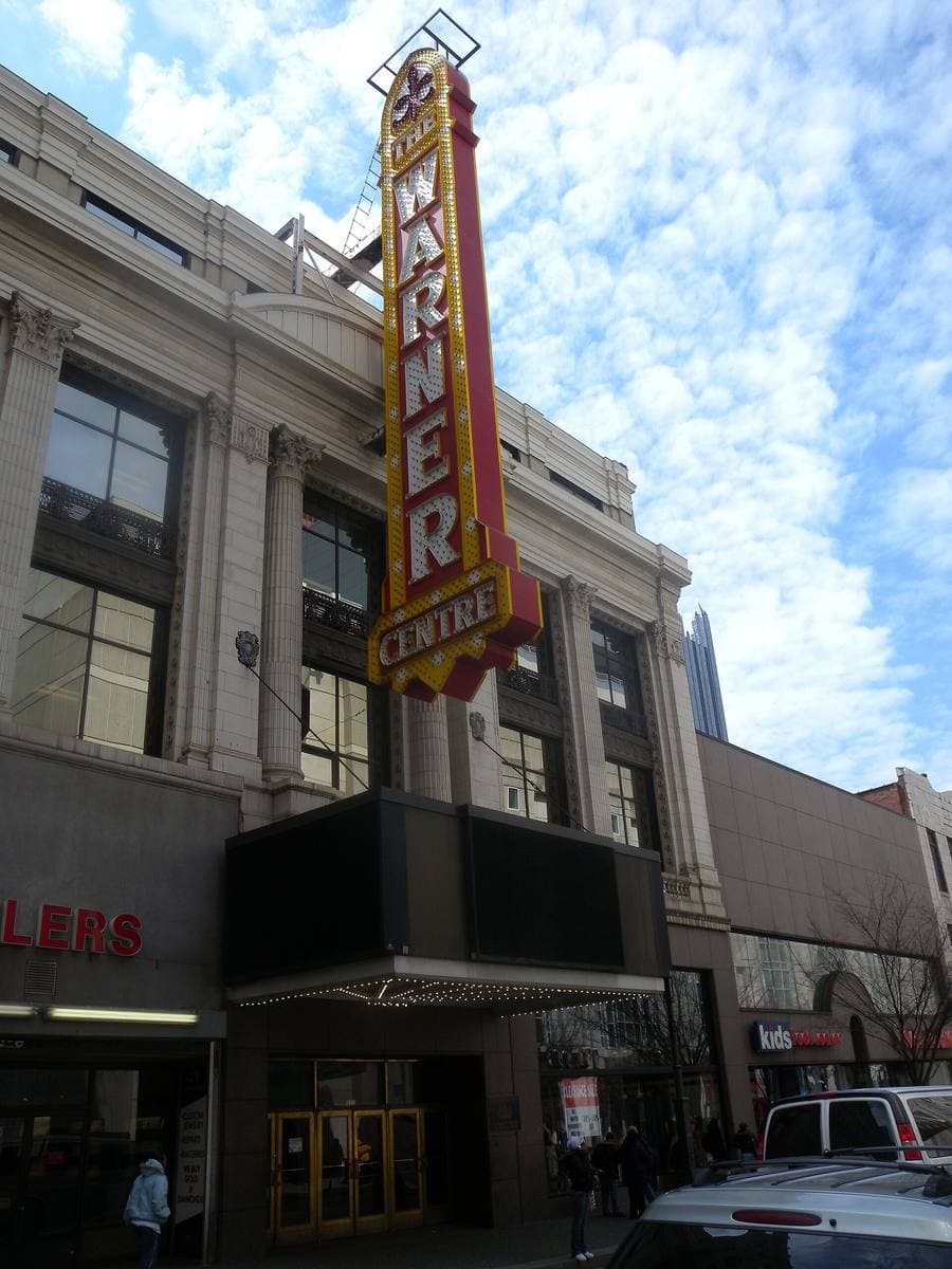 A tall vertical WARNER sign on a building front over a downtown street