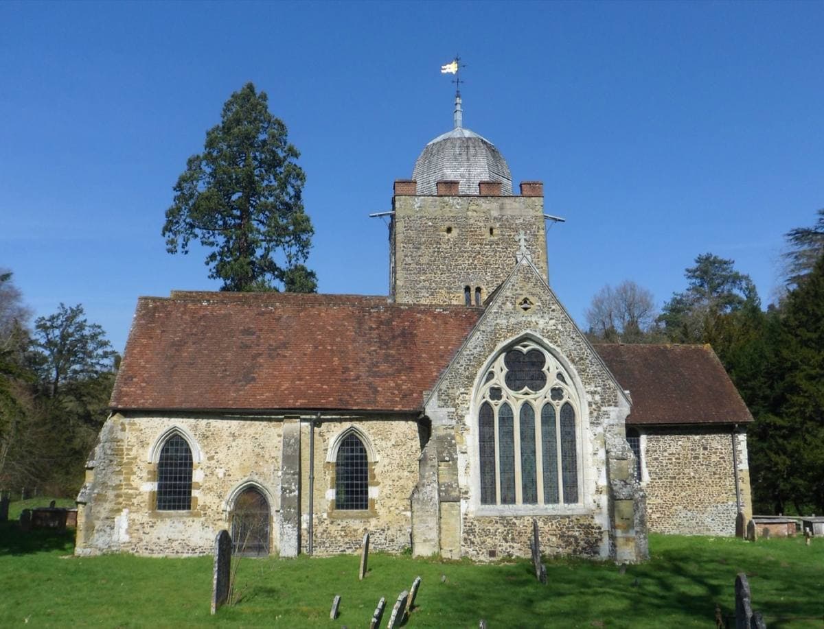 A small old church with a stone tower and a shingled cupola among trees