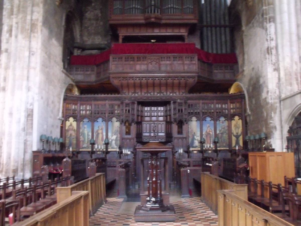 Carved wooden choir stalls and a lectern before a tall stone sanctuary with a red-fronted organ gallery