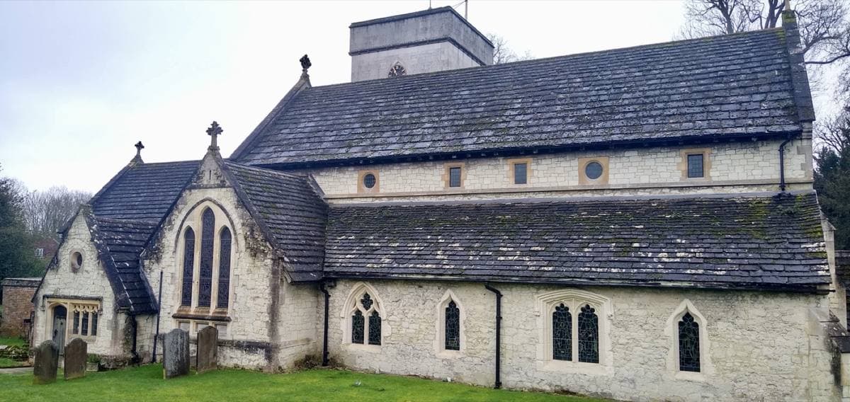 A flint and stone village church with a squat tower among churchyard trees