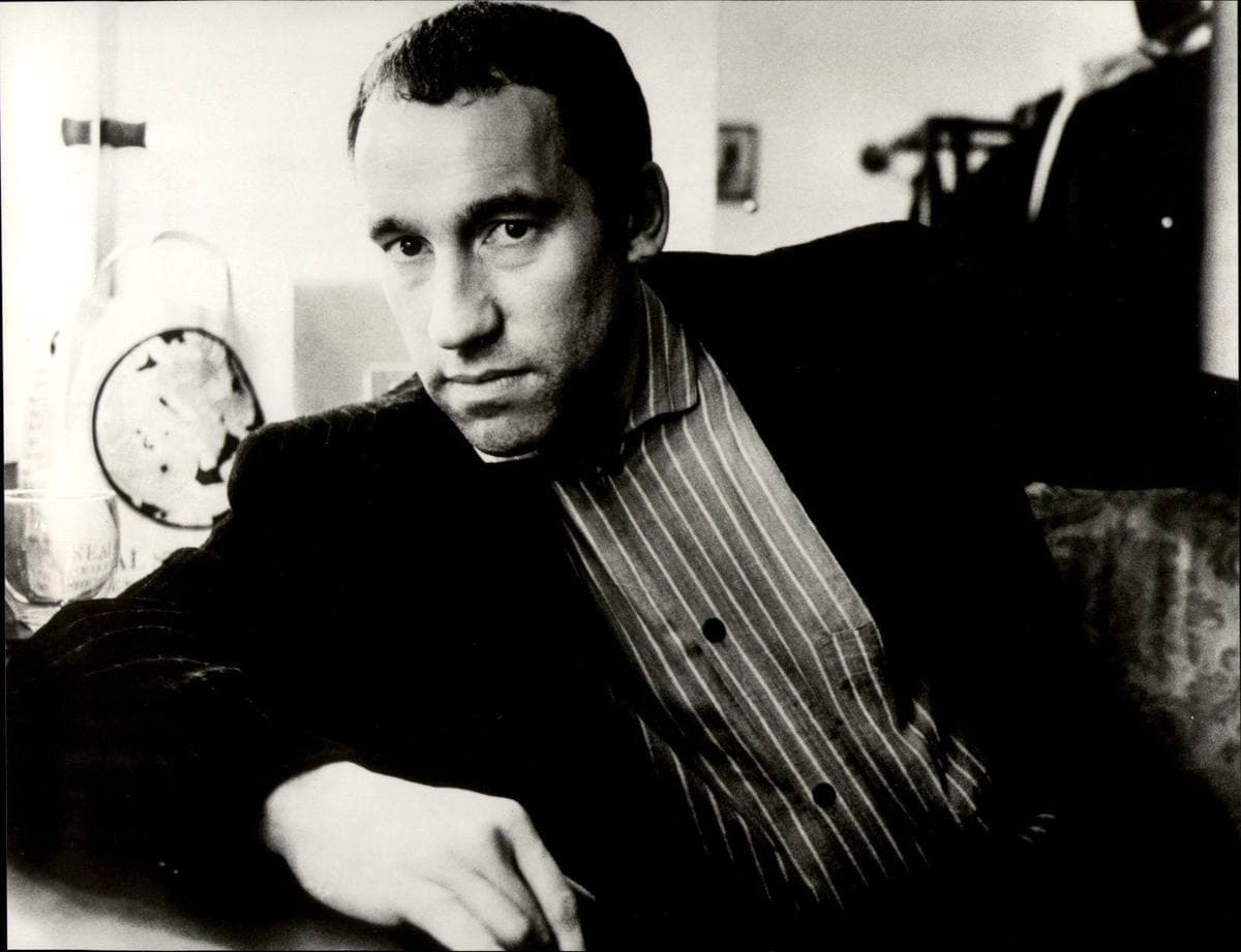 Black-and-white portrait of Simon Callow in a striped shirt, sitting in an armchair
