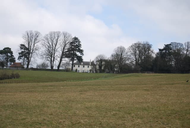 A large country house glimpsed behind a hedge and trees