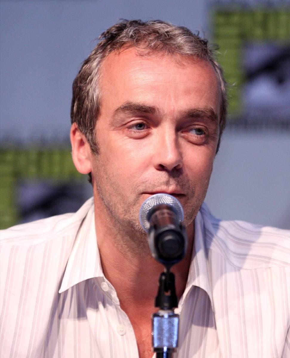 John Hannah speaking into a microphone, in a striped shirt