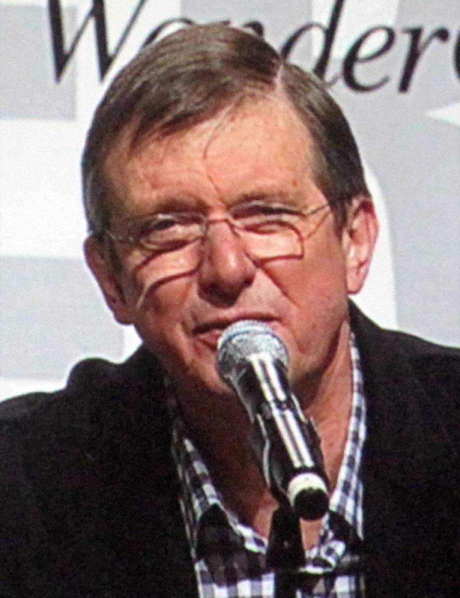 Mike Newell in glasses and a checked shirt, speaking into a microphone