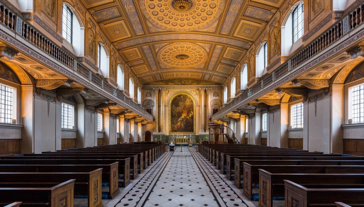 A pale chapel interior with a patterned marble floor, columns, a gallery and an ornate plaster ceiling