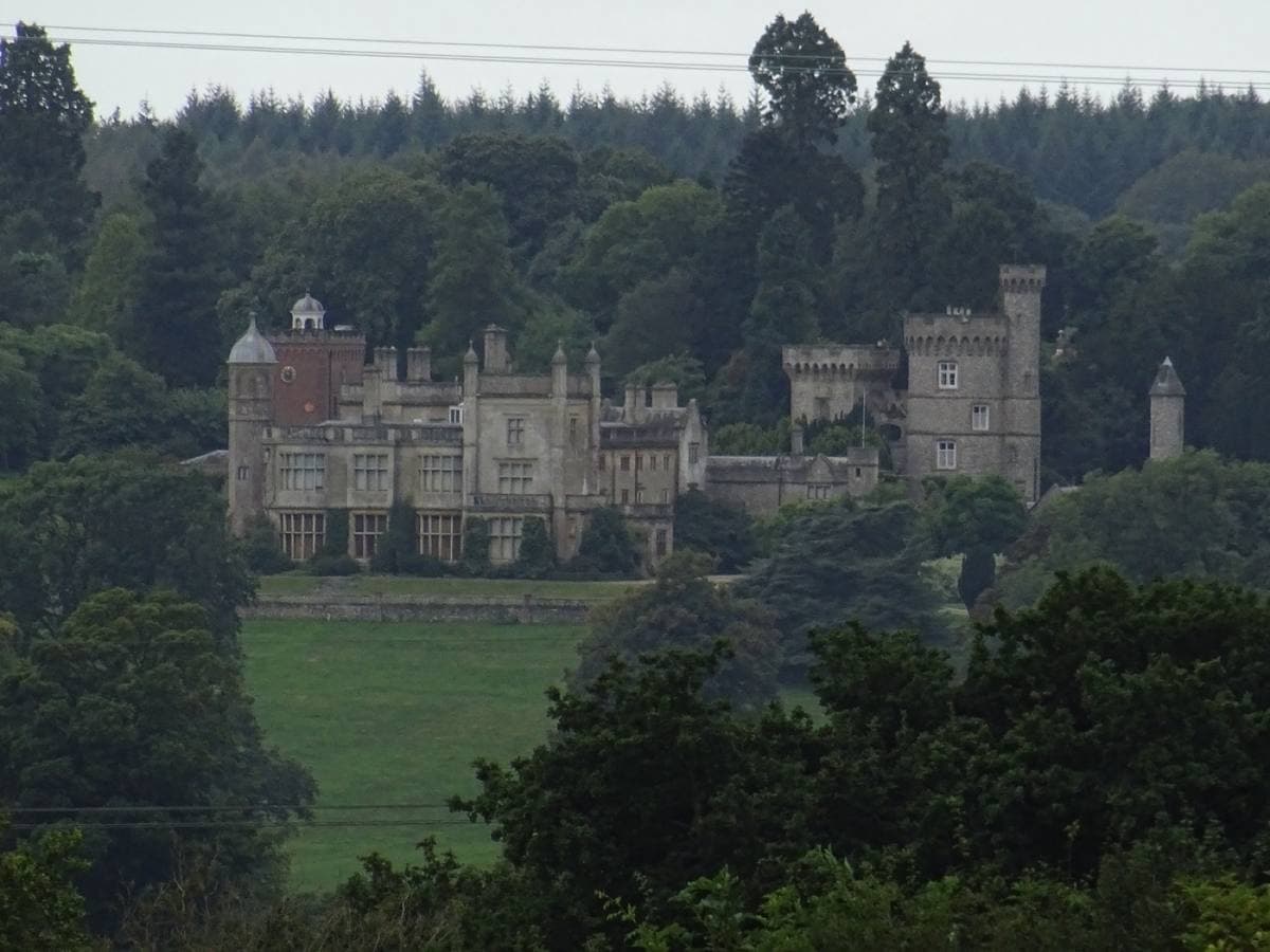 A grey stone Victorian Gothic house with towers and battlements above a lawn