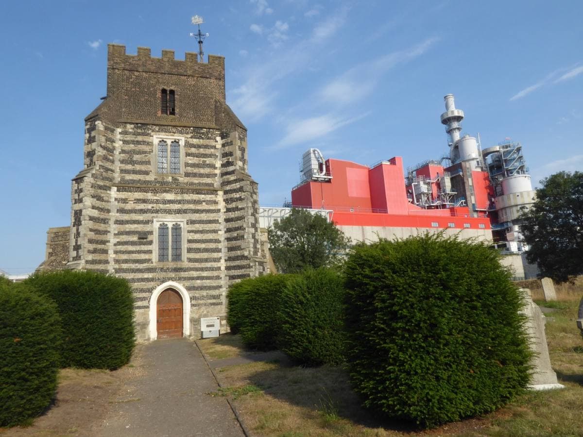 A small flint church with a chequered tower beside industrial buildings