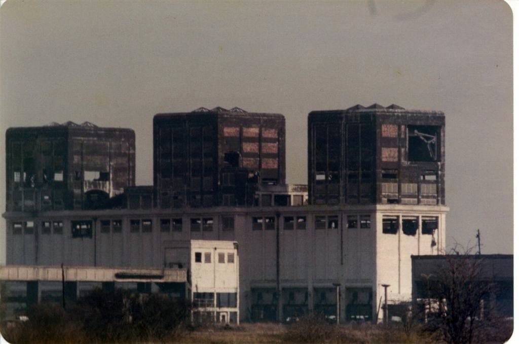 Three tall dark industrial blocks with broken windows on a long pale building