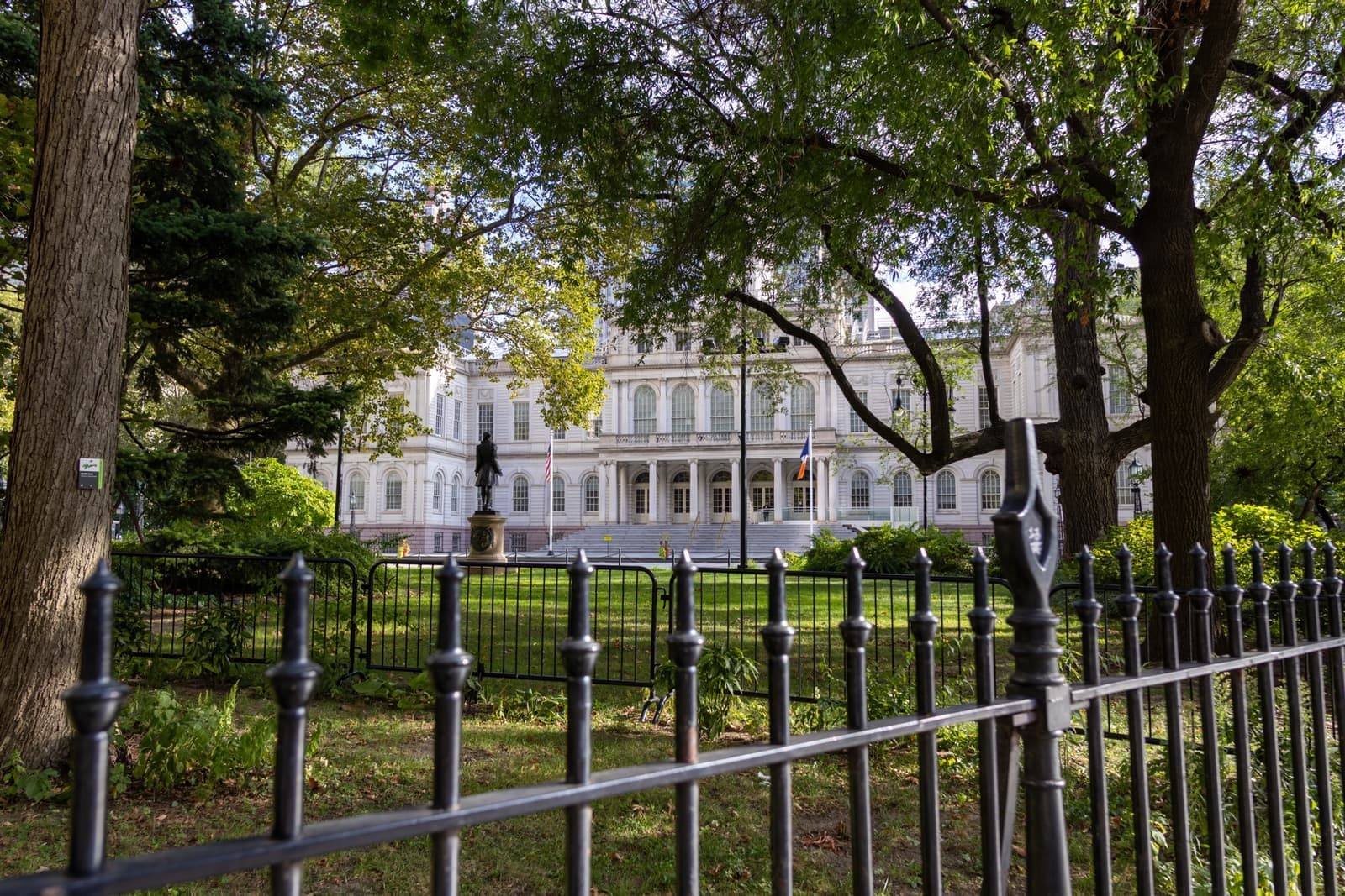 A white classical building behind trees and an iron fence