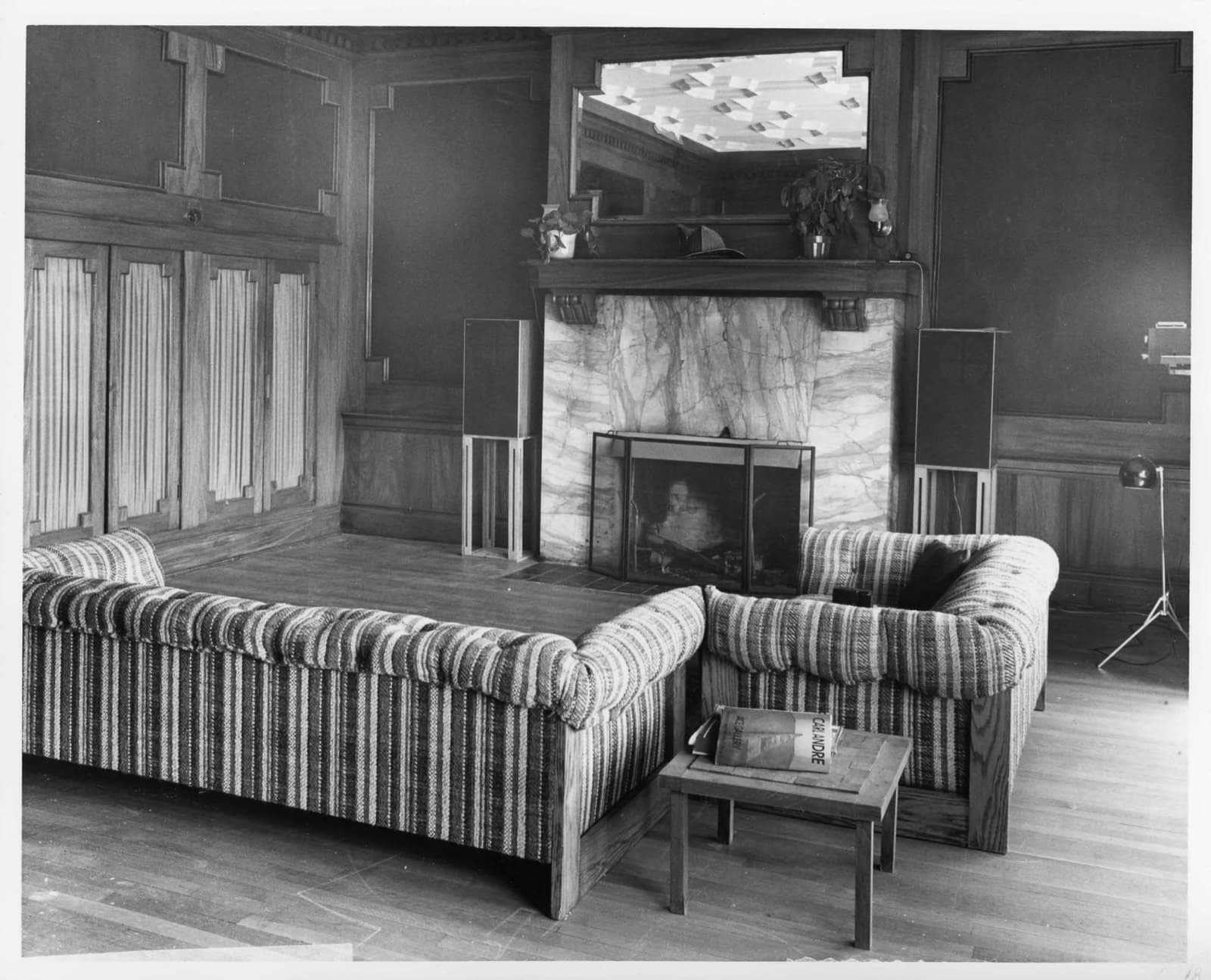 Black and white photograph of an old fire station room with a fireplace and striped sofa