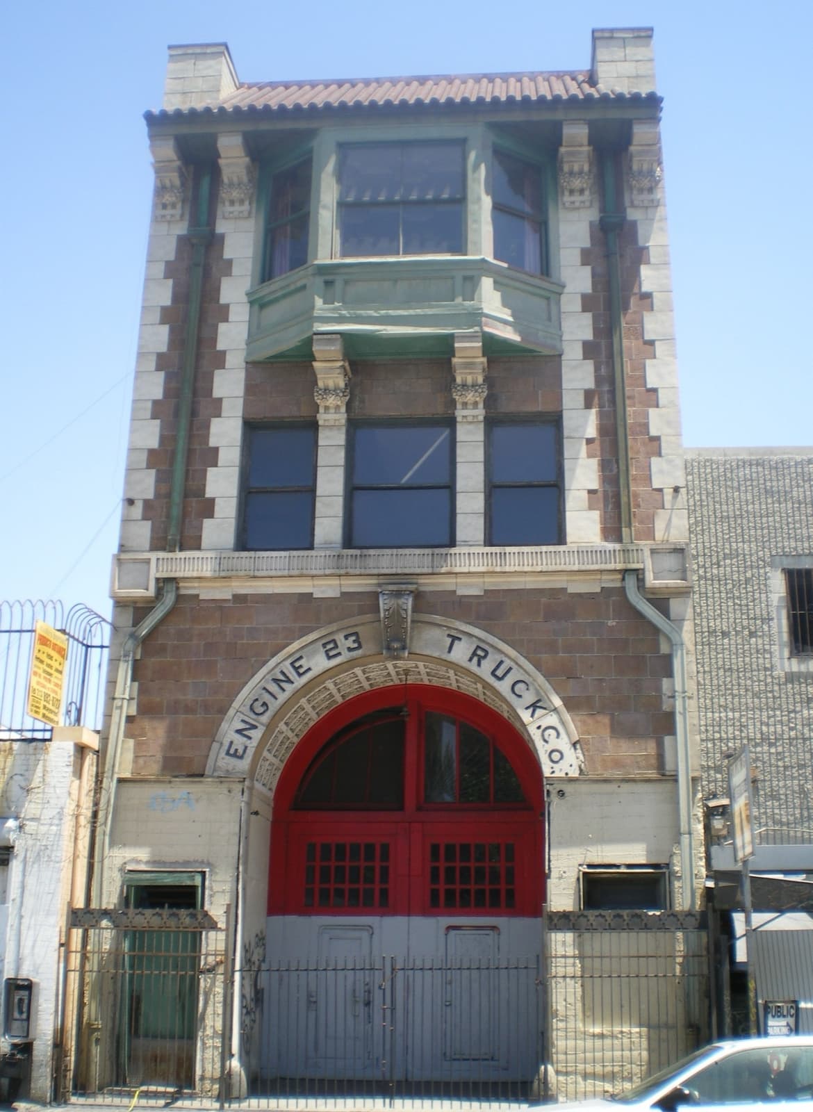 A tall, narrow brick fire station with a balcony and arched engine door