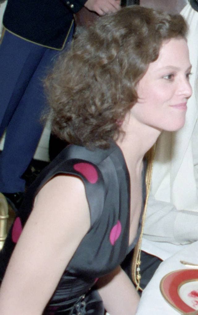 Sigourney Weaver with short curly hair, smiling, at a dinner table