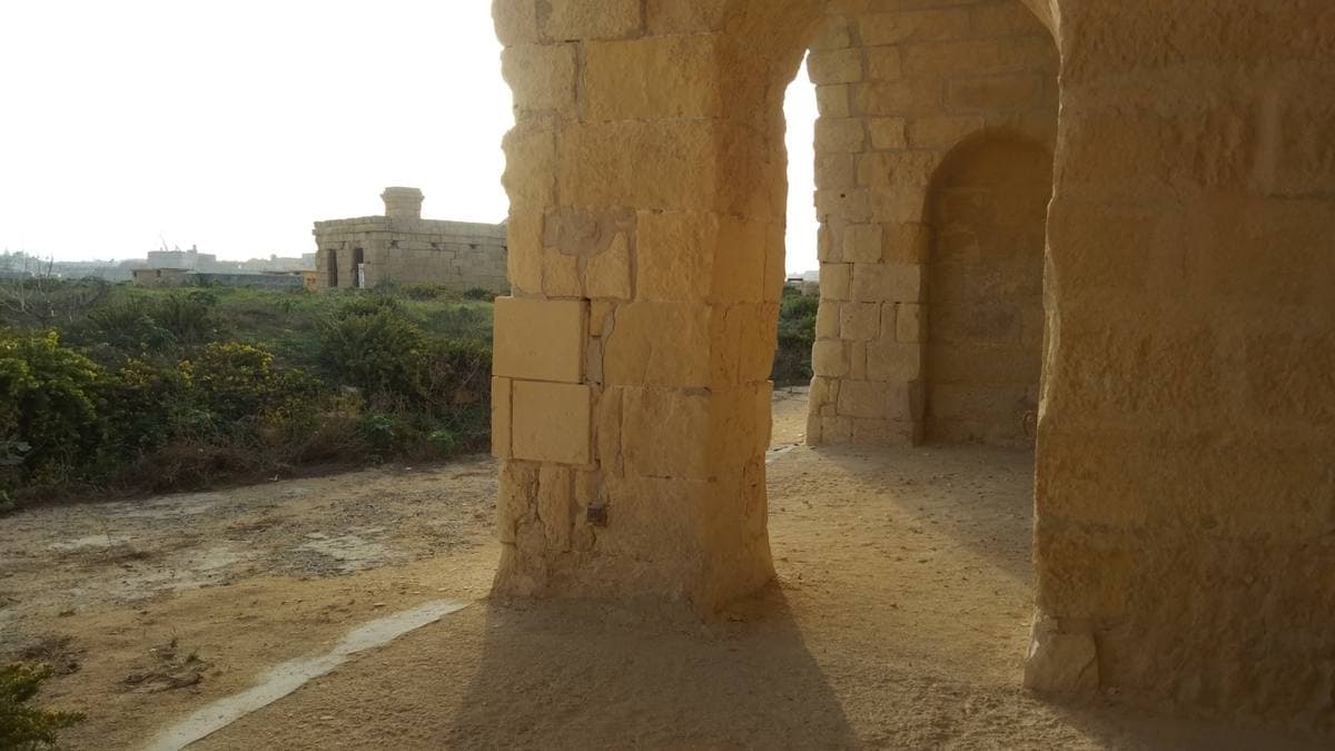 Sunlight falling through tall pale stone arches onto a sandy floor