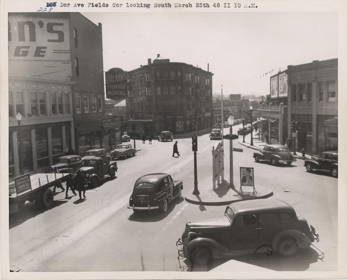 A busy city avenue with shop fronts and a rail overpass in 1948