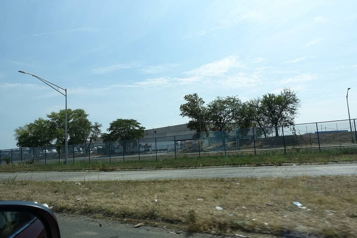Colour photograph of a fenced airport cargo area with trees and low buildings behind