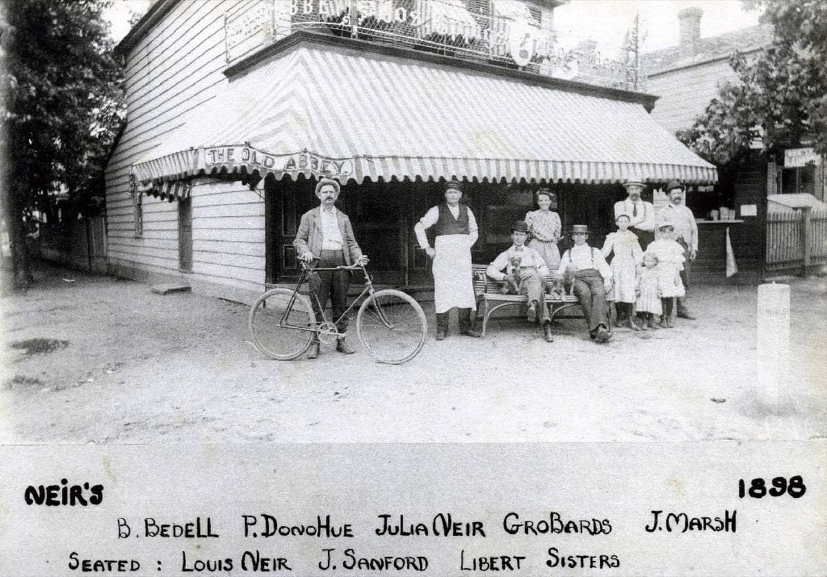 Black-and-white photograph of men in aprons and hats lined up outside a wooden tavern