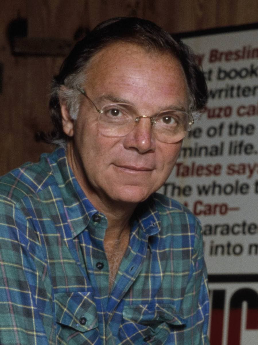 Colour photograph of Nicholas Pileggi in glasses and a checked shirt, in front of a newspaper cutting