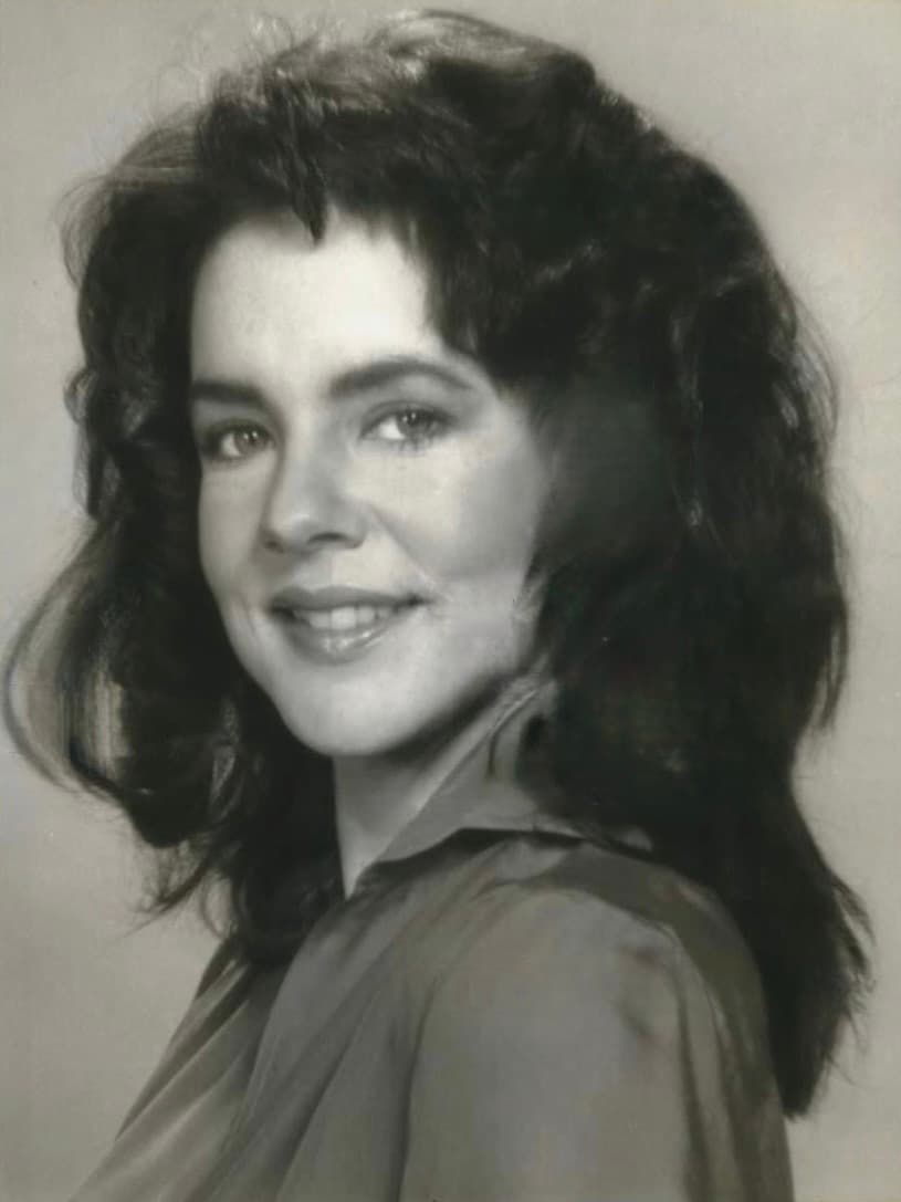 A smiling woman with dark wavy shoulder-length hair in a soft-focus studio portrait