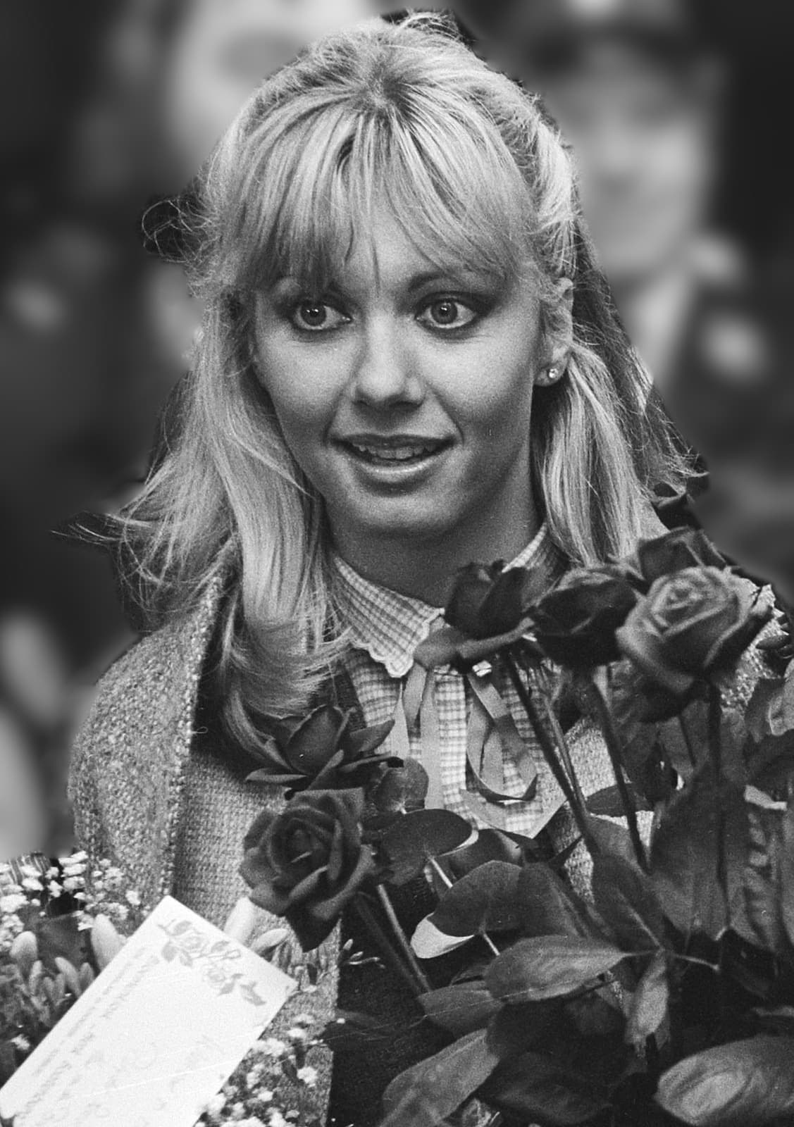 A young woman with fair, feathered hair and a fringe holding a bunch of red roses