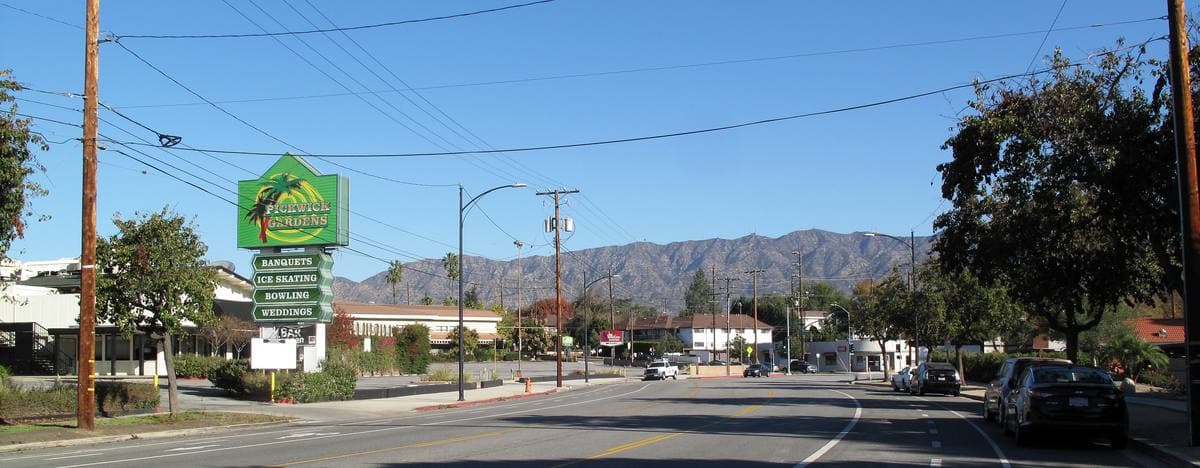 A sunny suburban road with a tall green Pickwick Gardens sign and mountains behind
