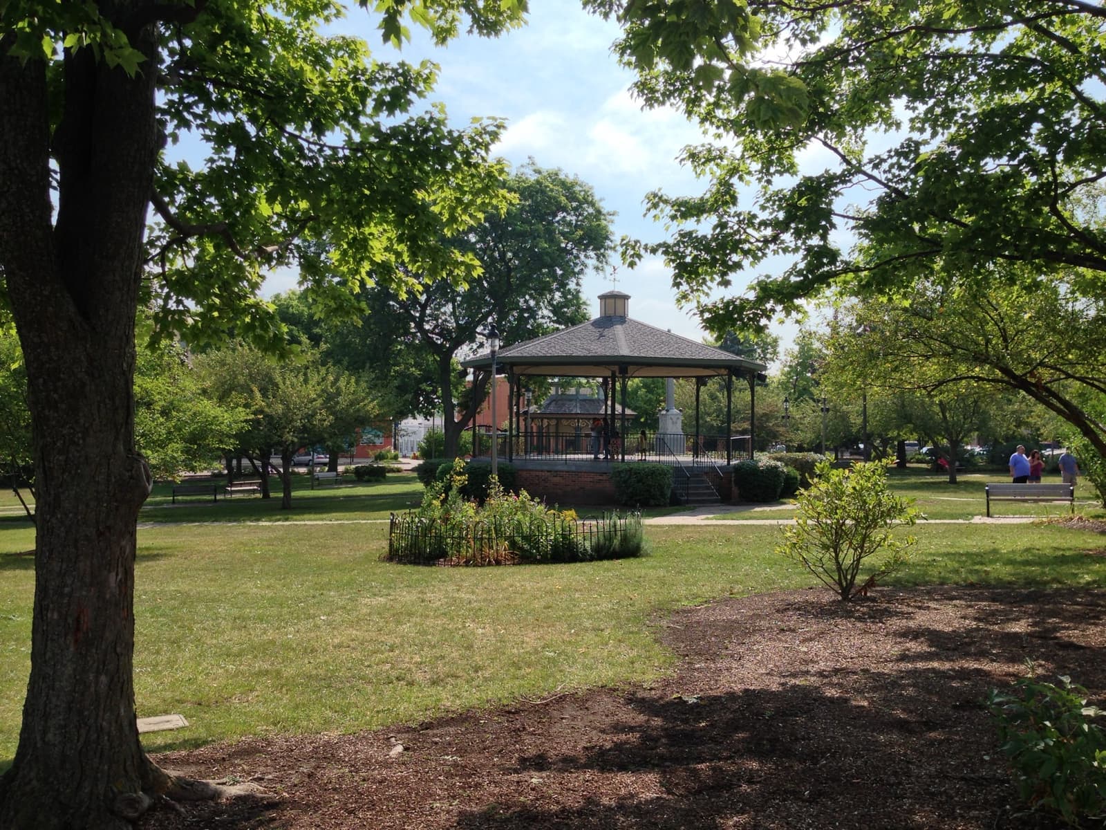 A green-roofed octagonal bandstand among trees and flower beds
