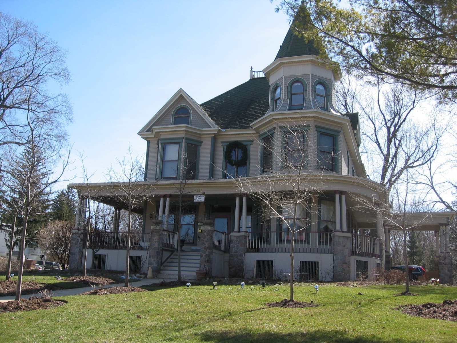 A grey Queen Anne house with a turret, a wraparound porch and a wreath