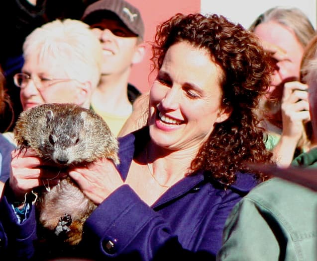 Andie MacDowell laughing as she holds a groundhog among photographers