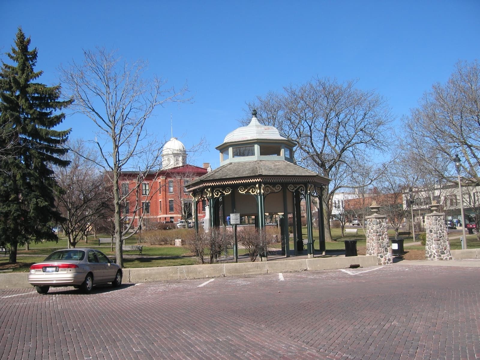 A brick-paved town square with bare trees, a white bandstand and a domed red-brick courthouse