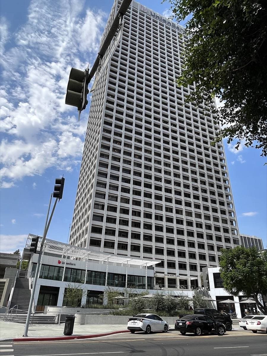A tall white grid-faced office tower at a street corner under a blue sky