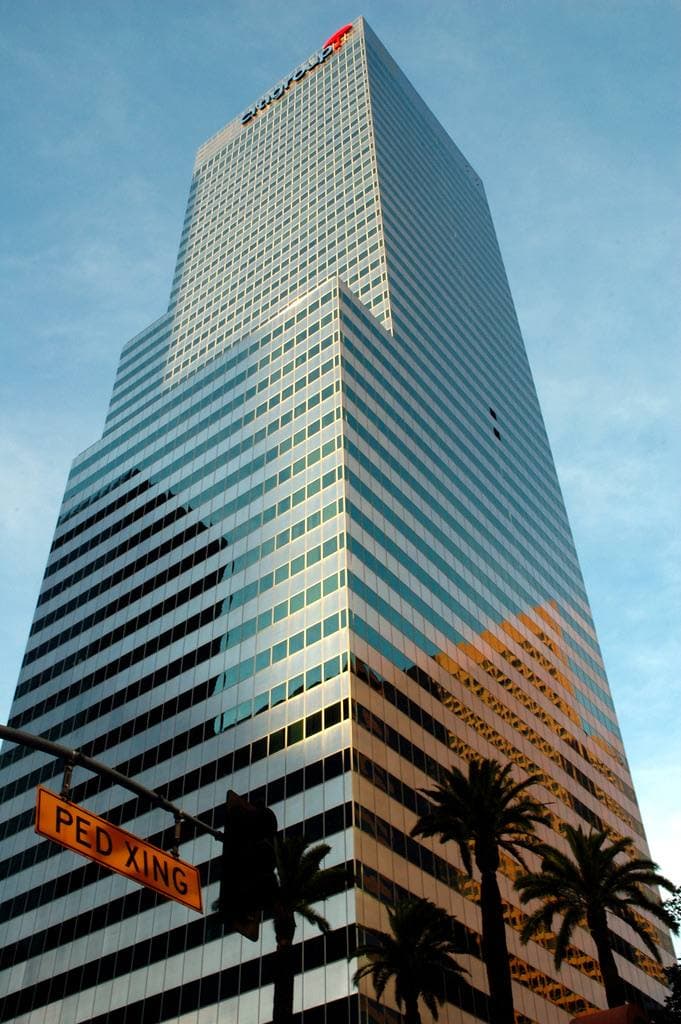 A dark glass office tower rising from palm trees, a Flower St street sign at the bottom