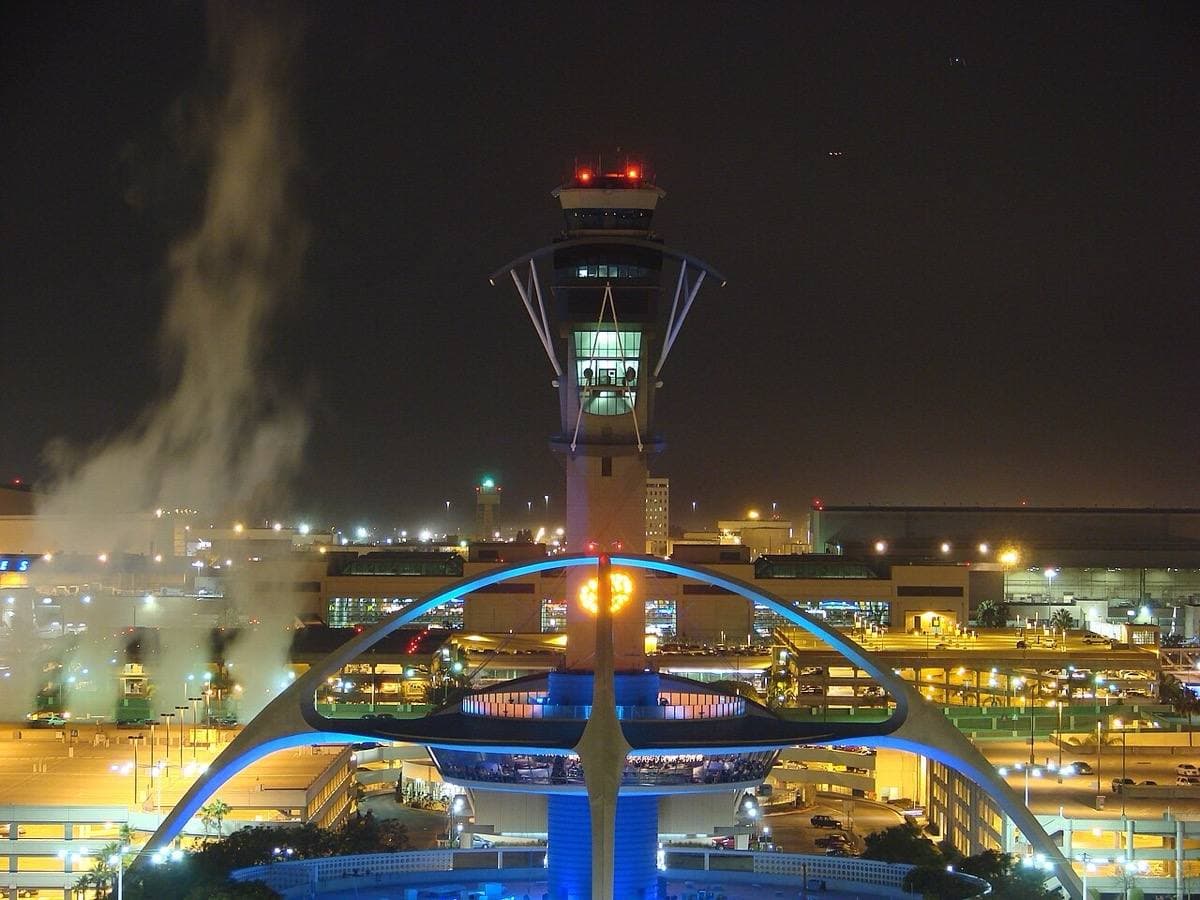 The arched Theme Building lit blue at night below the airport control tower