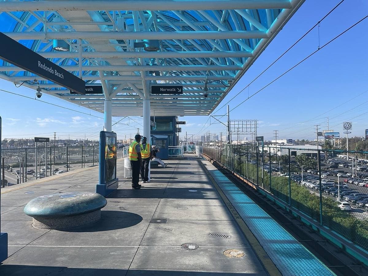 An elevated railway platform under a blue steel canopy with a train track beside it