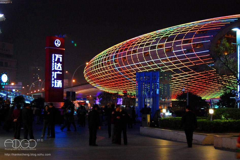 A huge egg-shaped lattice of coloured lights over a plaza at night