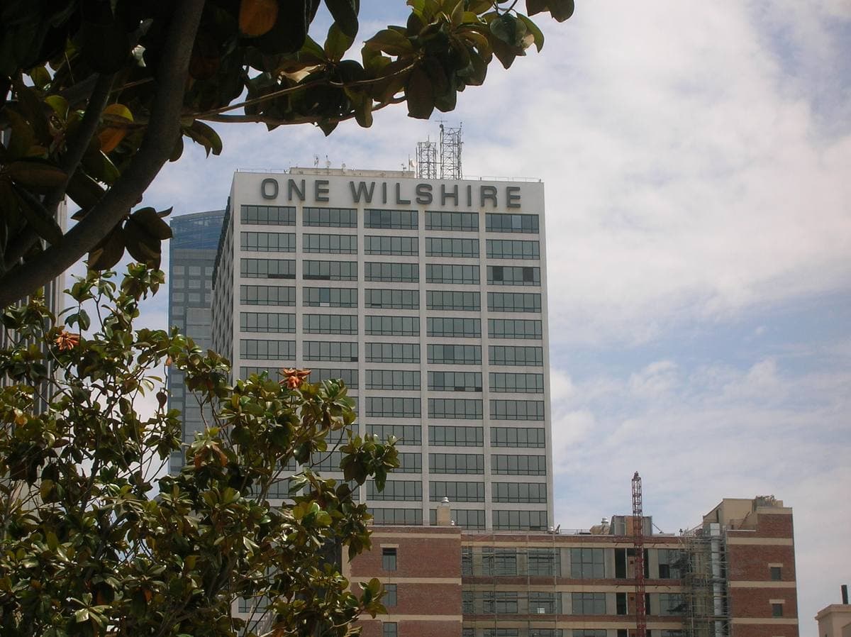 A pale office tower with ONE WILSHIRE on its roofline, seen through trees