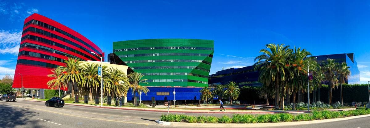 Three glass buildings in red, green and blue behind palm trees