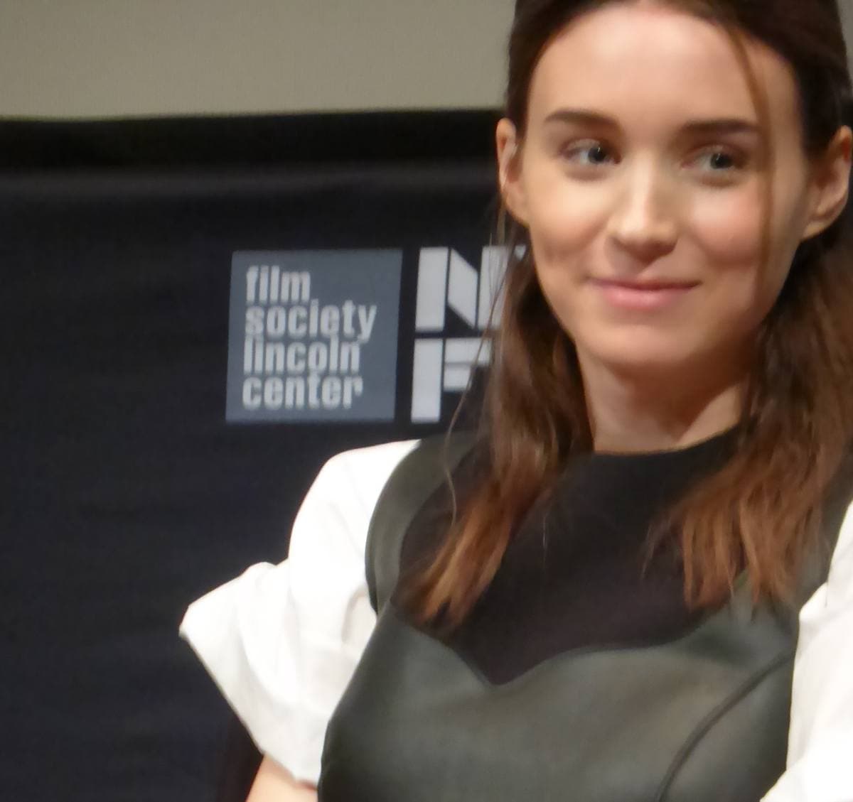 Rooney Mara with long dark hair, in black with white sleeves, seated with a microphone