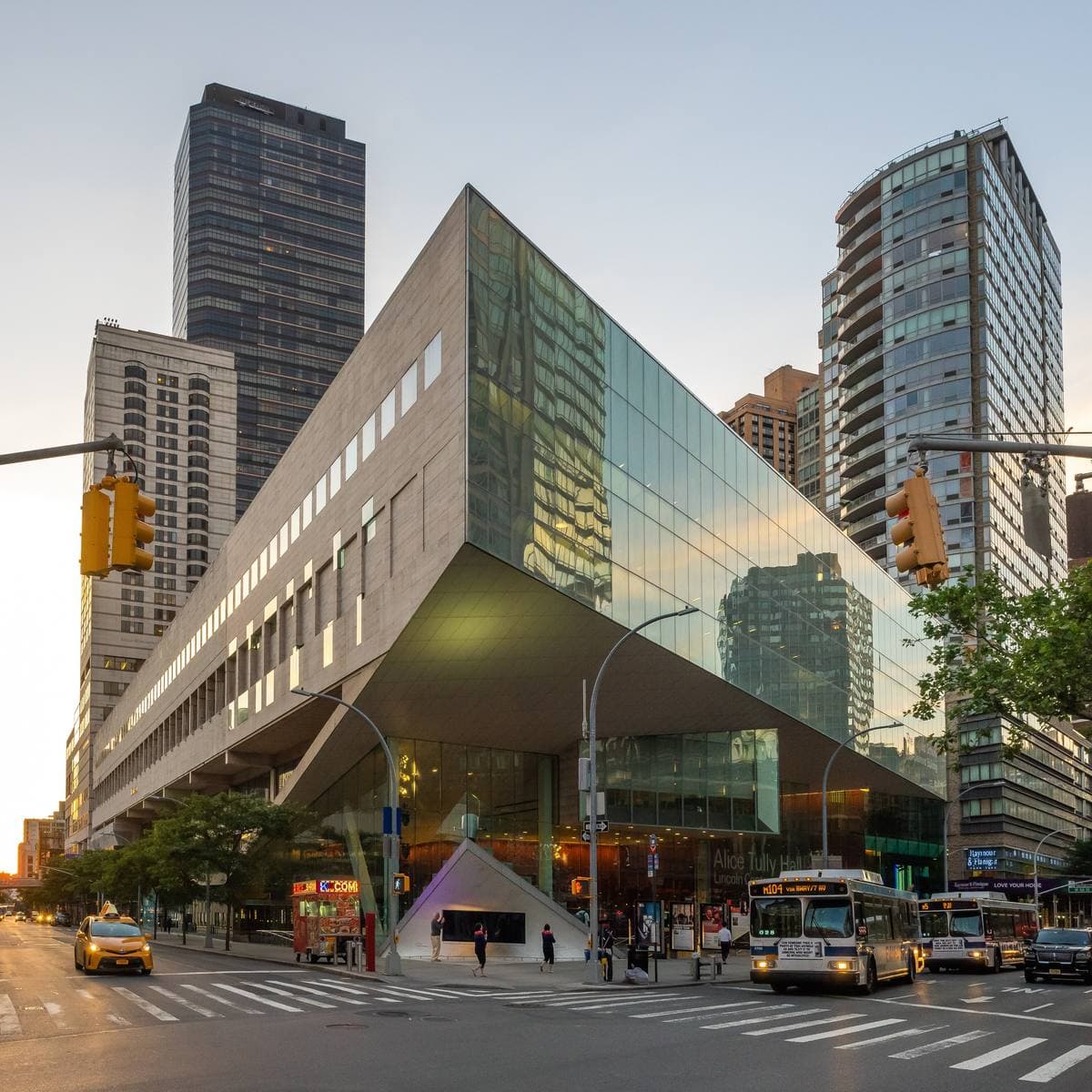 A glass-fronted hall under a sharply angled stone wing on a New York street corner