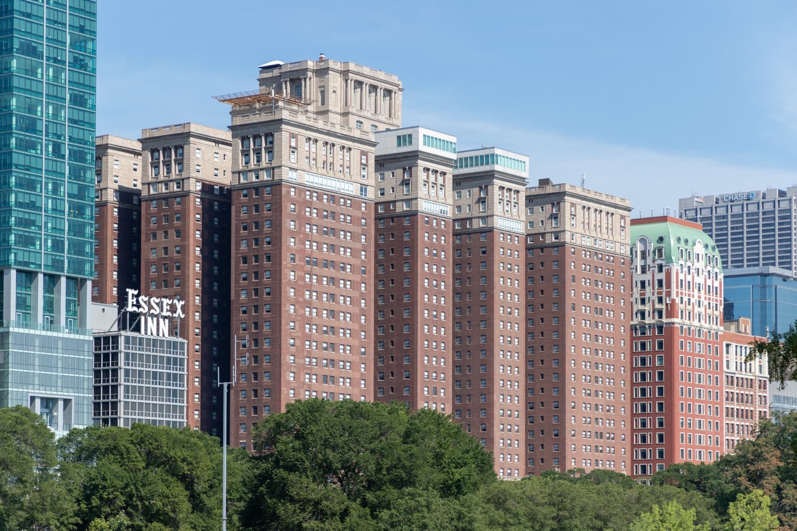 A long red-brick hotel with several towers rising behind park trees