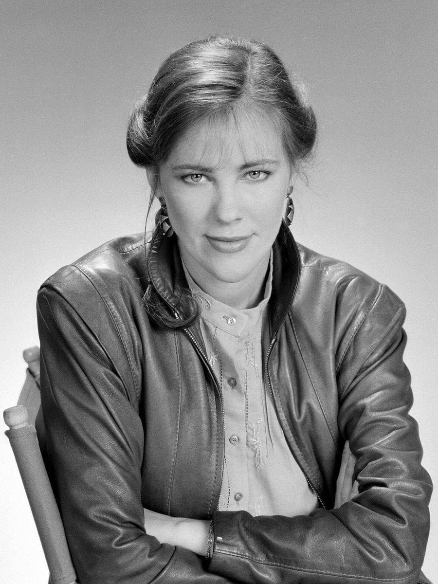 A young woman with tied-back hair in a leather jacket, arms folded, black and white