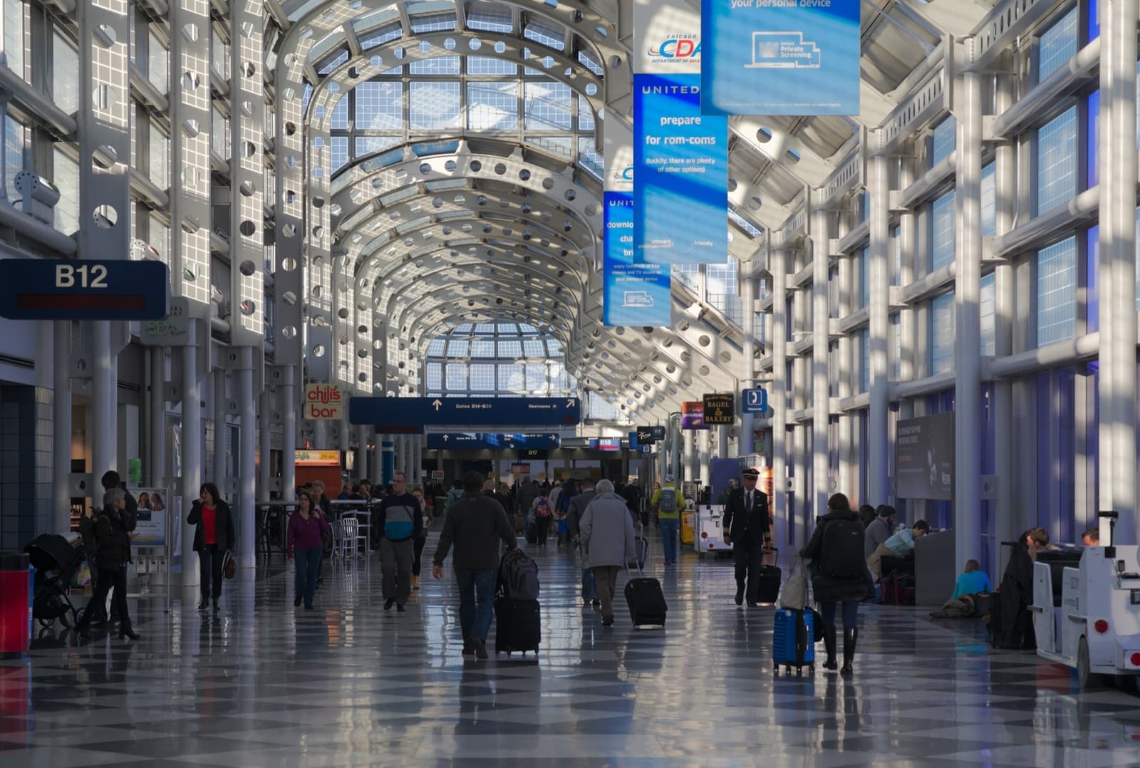 A long glass-roofed airport concourse with travellers and gate signs