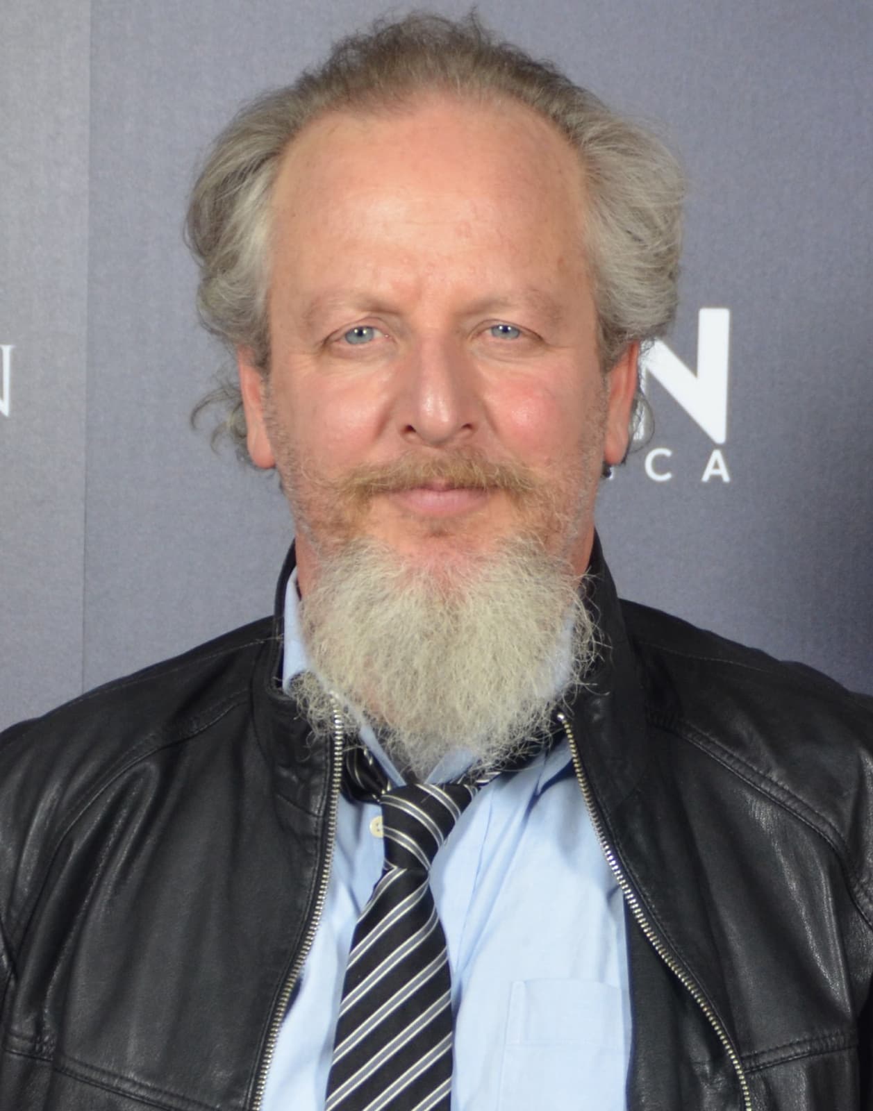 Daniel Stern with a long grey beard, in a leather jacket and tie