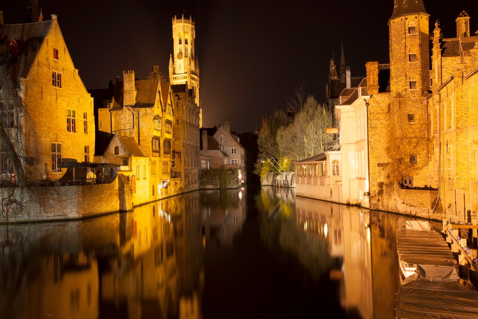 Floodlit gabled houses and the Belfry reflected in a canal at night
