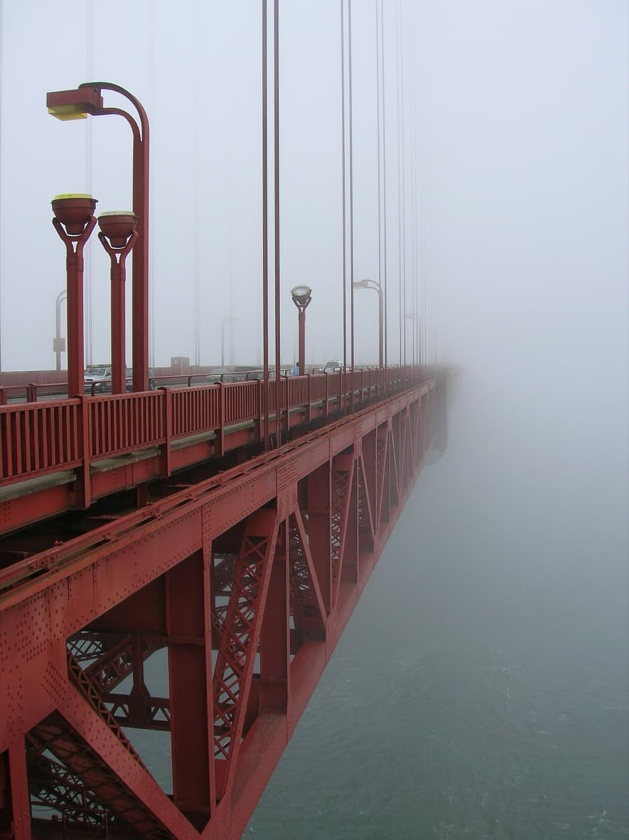 Fog rolling across the red towers of a suspension bridge